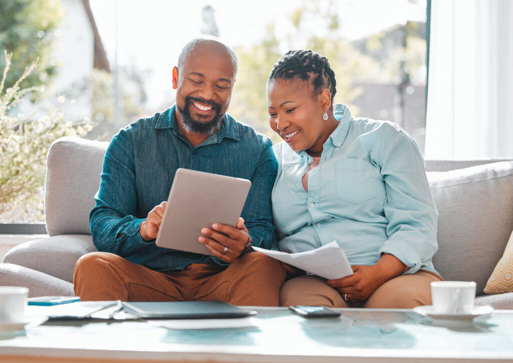 Technology, married couple with tablet and documents for pay their bills in a living room of their home. Finance or loan, budget or payment and black people with paper on a couch happy together.